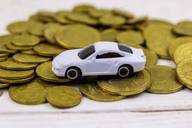 Beyaz ahşap arka plan üzerinde altın sikke yığını üzerinde Minyatür araba modeli