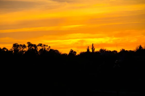Narancs naplemente körül sziluettek a falu és a fák — Stock Fotó