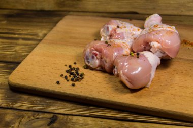 Çiğ tavuk bacağı ve ahşap masada baharatlar.