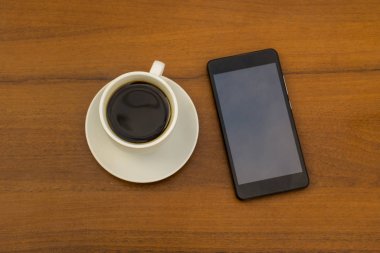 Ahşap masada bir fincan kahve ve akıllı telefon. Üst görünüm