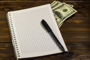 Tahta masanın üzerinde tükenmez kalem ve dolar banknotları olan defter. Para biriktirme kavramı