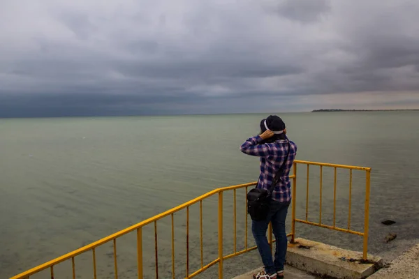 Ung kvinna i rutig skjorta stående på stranden ensam och tittar på havet i en dyster grå dag. Bakifrån — Stockfoto