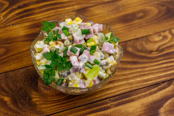 Вкусный салат с колбасой, зеленым горошком, консервированной кукурузой, перцем, огурцом и майонезом на деревянном столе — стоковое фото