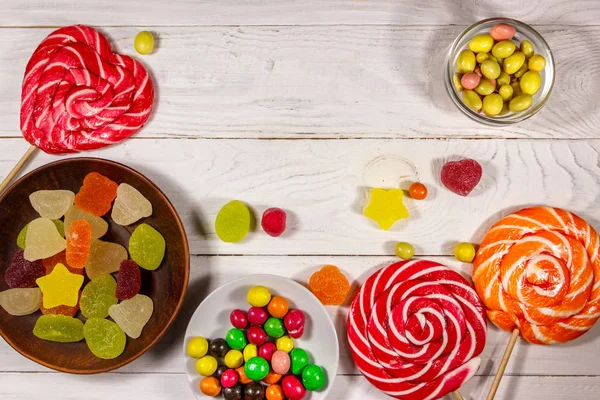 Барвисті шоколадні цукерки, льодяники та желе на білому дерев'яному столі — стокове фото