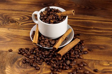 Beyaz fincan kahve çekirdekleri ve tarçın ahşap masada sopalar 