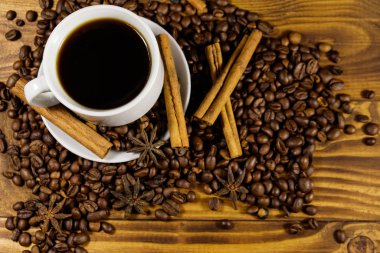 Bir fincan kahve, kavrulmuş kahve çekirdekleri, yıldız anason ve ahşap masada tarçın çubukları. Üst görünüm