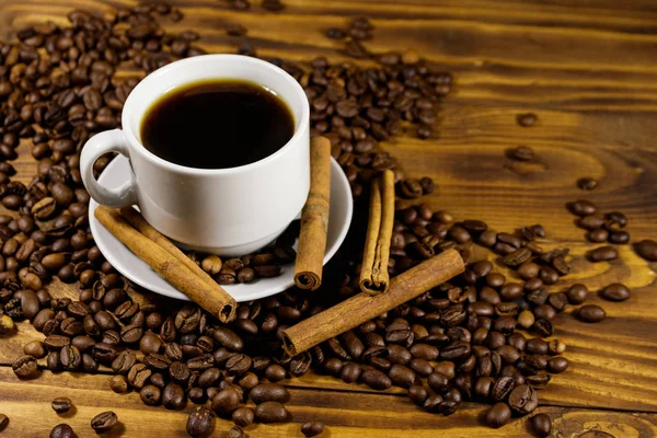 Taza de café, granos de café tostados y palitos de canela en la mesa de madera —  Fotos de Stock