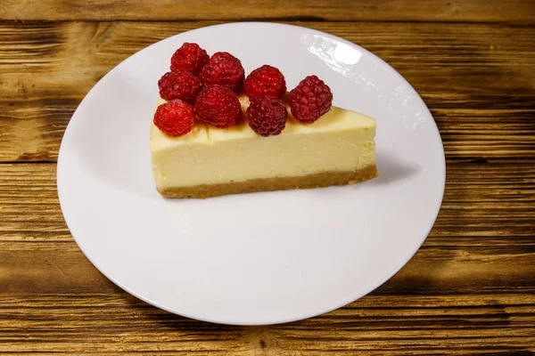 Piece of tasty New York cheesecake with raspberries in a white plate on wooden table — Stock Photo, Image