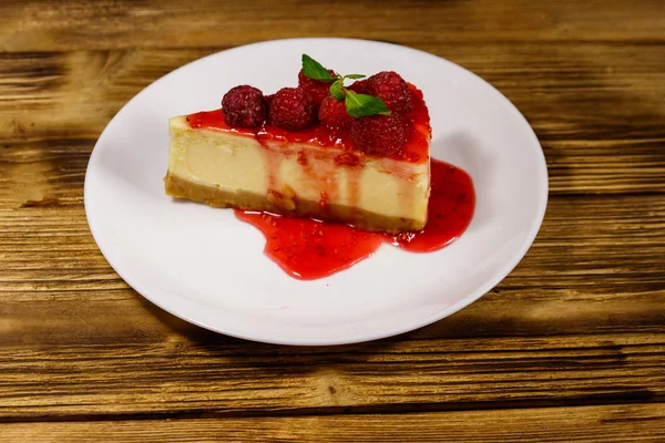 Piece of tasty New York cheesecake with raspberries and raspberry jam in a white plate on wooden table — Stock Photo, Image