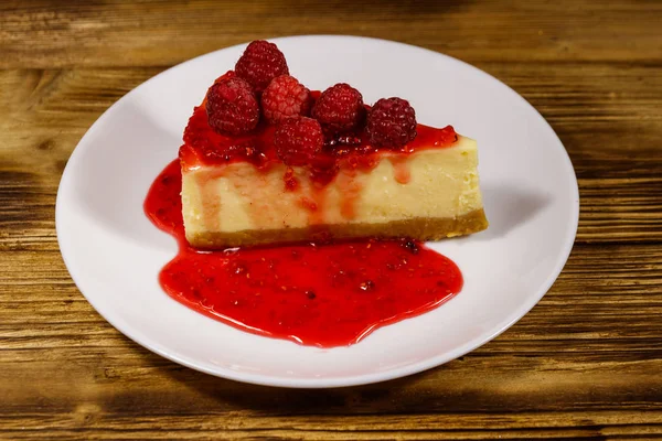 Piece of tasty New York cheesecake with raspberries and raspberry jam in a white plate on wooden table — Stock Photo, Image