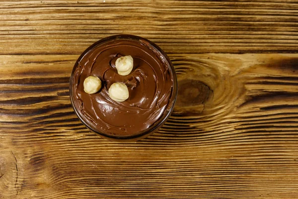 Ciotola di vetro con deliziosa nocciola al cioccolato spalmata su tavolo di legno. Vista dall'alto — Foto Stock