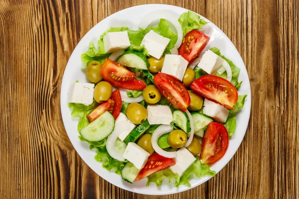 Ελληνική σαλάτα με φρέσκα λαχανικά, φέτα και πράσινες ελιές σε ξύλινο τραπέζι. Άνω όψη — Φωτογραφία Αρχείου