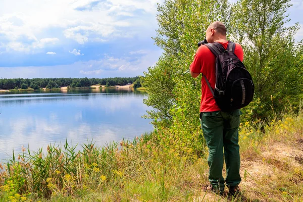 Ung resenär man med ryggsäck tar ett foto av sjön. Rese fotografi koncept — Stockfoto
