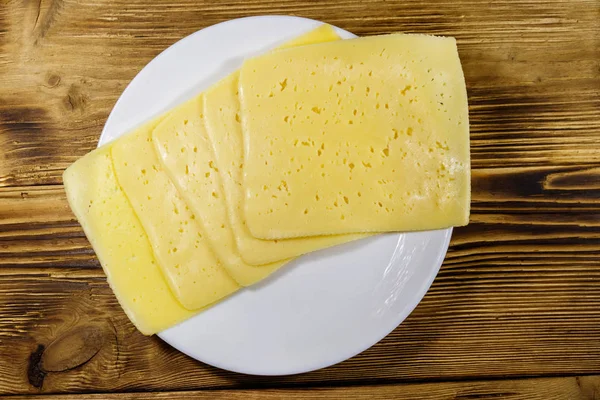 Rebanadas de queso en un plato sobre una mesa de madera. Vista superior —  Fotos de Stock