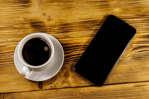 Cup of coffee and smartphone on a wooden table — Stock Photo, Image