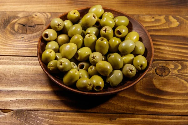 Placa con aceitunas verdes sobre mesa de madera — Foto de Stock