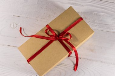 Beyaz ahşap masa üzerinde kırmızı kurdele ile karton hediye kutusu