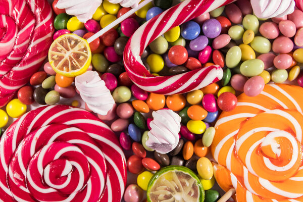 Background of colorful chocolate candies, lollipops, candy cane and marshmallows