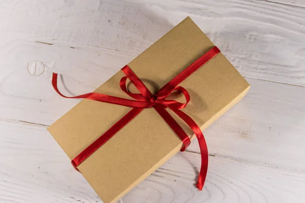 Tekturowe pudełko z czerwoną wstążką na biały drewniany stół — Zdjęcie stockowe