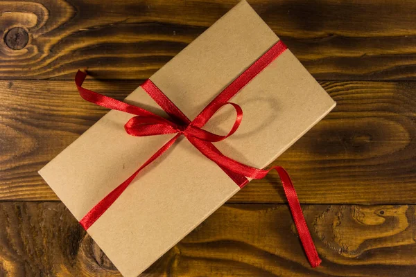 Χάρτινο κουτί δώρου με κόκκινη κορδέλα σε ξύλινο τραπέζι — Φωτογραφία Αρχείου