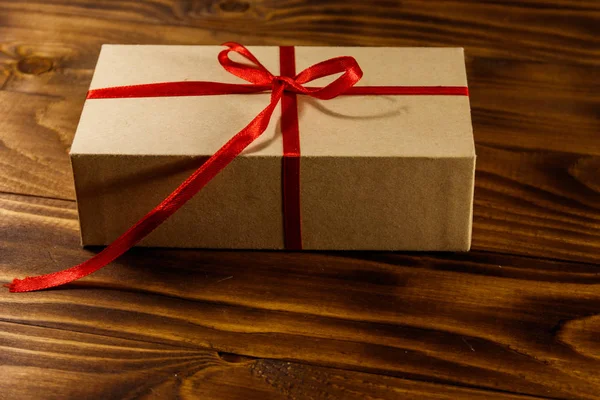 Caja de regalo de cartón con cinta roja sobre mesa de madera — Foto de Stock