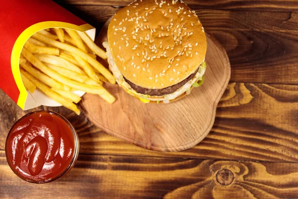 Delizioso hamburger grande con patatine fritte e ketchup sul tavolo di legno. Vista dall'alto — Foto Stock