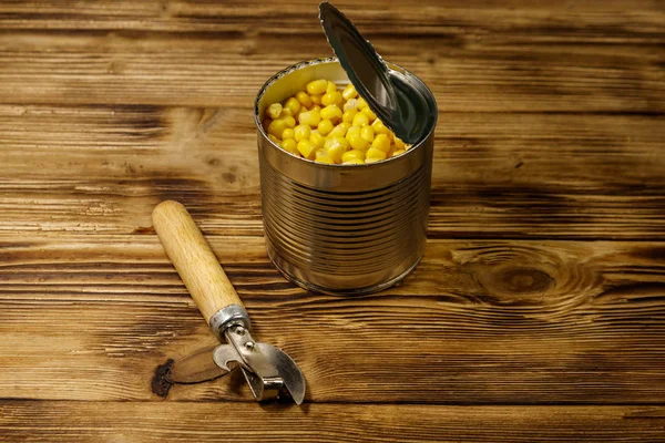 Open tin can of corn and can opener on wooden table — Stock Photo, Image