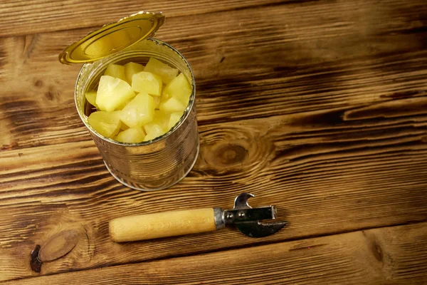 Lata abierta de pedazos de piña y abrelatas en mesa de madera —  Fotos de Stock