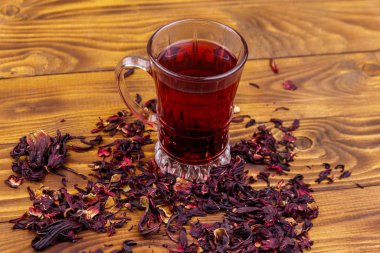 Ahşap masada bir bardak kırmızı amber çayı (carcade, roselle).