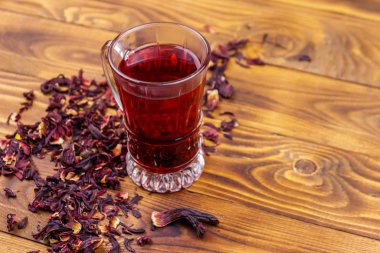 Ahşap masada bir bardak kırmızı amber çayı (carcade, roselle).