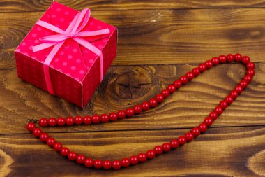 Ahşap arka plan üzerinde hediye kutusu ve kırmızı boncuk kolye