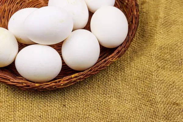 White chicken eggs in wicker basket on sackcloth background — Stock Photo, Image