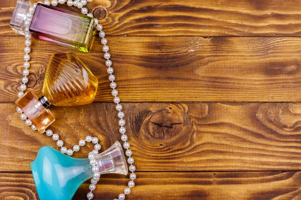 Różne butelki perfum i perłowy naszyjnik na drewnianym tle. Widok z góry, Kopiuj spację — Zdjęcie stockowe