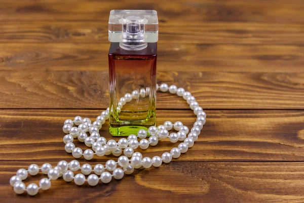 Bottle of perfume and pearl necklace on wooden background Royalty Free Stock Images