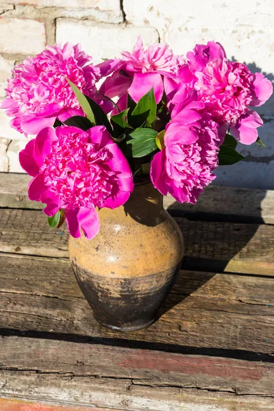 Bouquet of pink peony flowers in clay jug on rustic wooden table — Stock Photo, Image