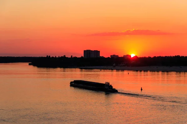 Tugboat duwt een zware lange boot op de rivier de Dnjepr bij zonsondergang — Stockfoto