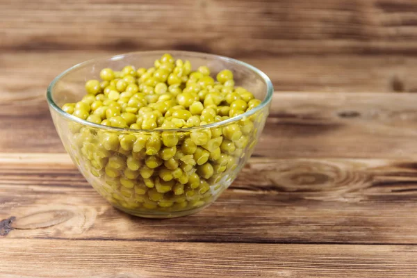 Ingeblikte groene erwten in glazen kom op houten tafel — Stockfoto