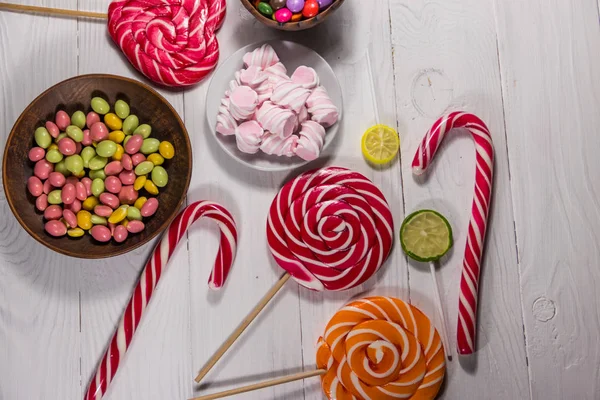Colorful chocolate candies, lollipops, candy cane and marshmallows on white wooden table — Stock Photo, Image