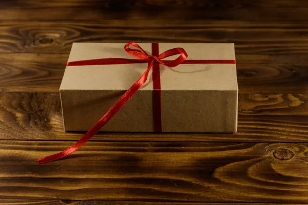 Caja de regalo de cartón con cinta roja sobre mesa de madera — Foto de Stock