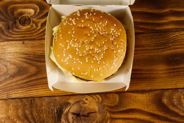 Heerlijke grote hamburger in kartonnen doos op houten tafel — Stockfoto