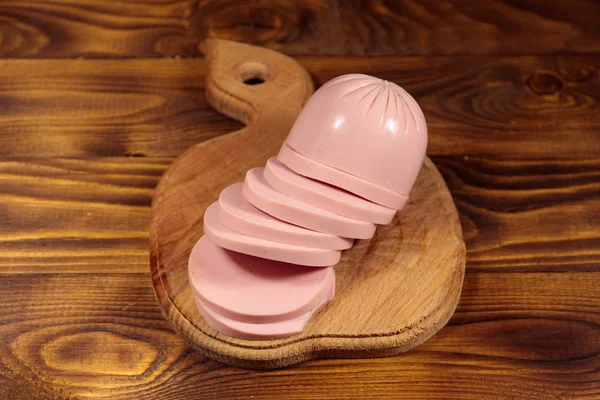 Sliced boiled sausage on cutting board on wooden table — Stock Photo, Image