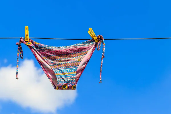 Traje de baño femenino de secado colgado de una cuerda contra el cielo azul — Foto de Stock