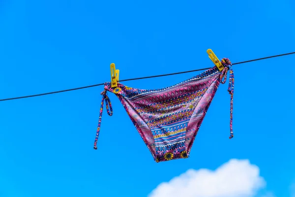 Traje de baño femenino de secado colgado de una cuerda contra el cielo azul — Foto de Stock