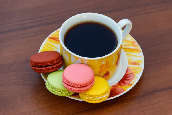 Tasse Kaffee mit leckeren bunten Macarons auf Holztisch — Stockfoto