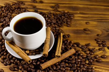 Bir fincan kahve, kavrulmuş kahve çekirdekleri ve ahşap masada tarçın çubukları.