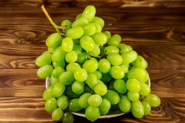 Gustosa uva bianca fresca in un piatto sul tavolo di legno — Foto Stock