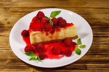 Ahududu ve ahududu reçelli lezzetli New York peynirli keki ahşap masada beyaz bir tabakta.