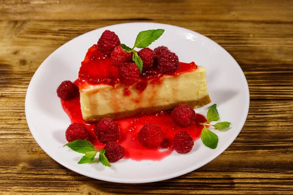 木製のテーブルの上に白いプレートにラズベリーとラズベリージャムとおいしいニューヨークチーズケーキのピース — ストック写真