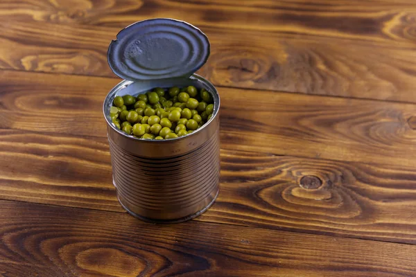 Open tin can of green peas on wooden table — Stock Photo, Image