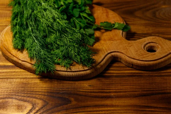 Eneldo verde fresco y perejil en tabla de cortar en mesa de madera —  Fotos de Stock